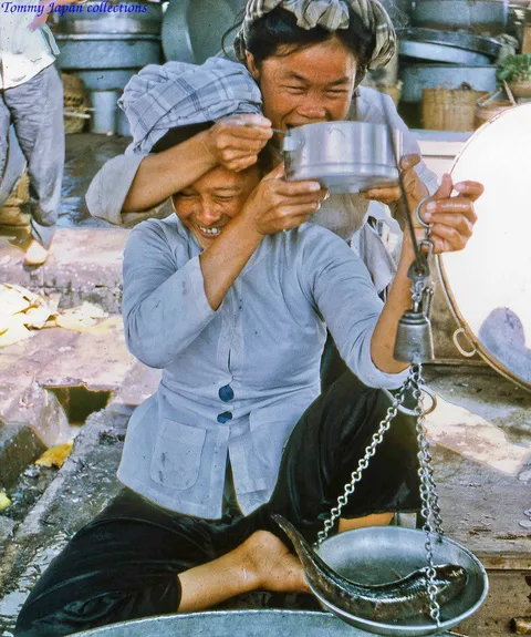 alt: Hai người bán cá dựa giỏ khi được chụp hình