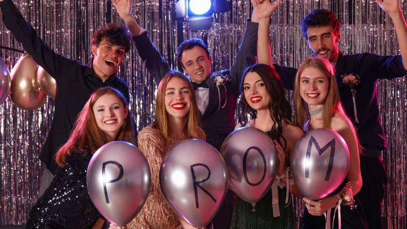 Một nhóm học sinh trung học mặc trang phục dạ hội đang cười nói và chụp ảnh cùng nhau tại một buổi prom. Không khí vui tươi và trang trọng.