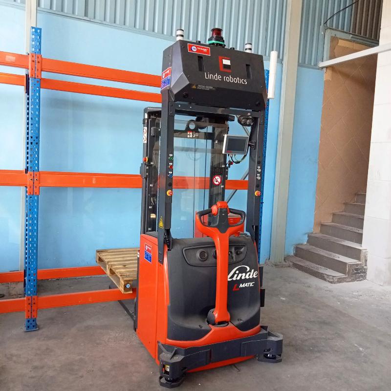 Xe nâng tay inox màu bạc đang nâng một pallet chứa các thùng hàng màu xanh lam trong kho